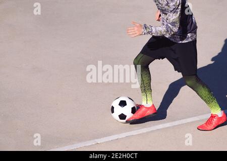 les jambes d'un joueur de football méconnaissable qui joue avec le ballon dans un terrain de football en béton, le concept de style de vie sain et le sport urbain dans la ville, Banque D'Images