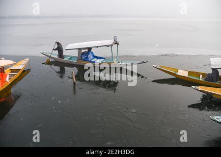 Srinagar, Inde. 14 janvier 2021. Un homme délague son bateau shikara sur un lac de dal partiellement gelé pendant une matinée hivernale froide à Srinagar.mercredi, les températures nocturnes se sont encore effondrées dans la vallée du Cachemire avec un dépôt de mercure à moins 8.4°C à Srinagar, La température la plus basse de cette saison jusqu'à présent et la nuit de janvier la plus froide des 25 dernières années, ont déclaré les responsables jeudi. Crédit : SOPA Images Limited/Alamy Live News Banque D'Images