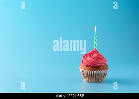 Gâteau d'anniversaire rose avec bougie verte sur fond bleu Banque D'Images