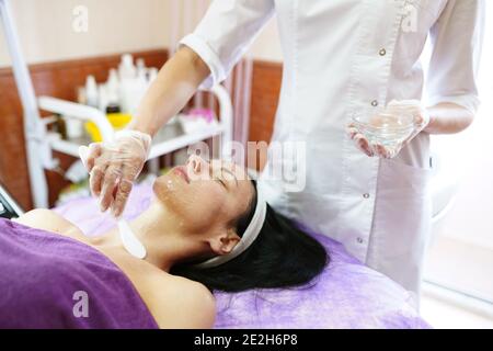 Un cosmétologue professionnel applique un masque sur le visage du client dans un salon de spa. Belle femme sur une procédure de cosmétologie. Centre de bien-être Banque D'Images
