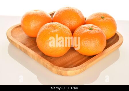 Quelques mandarines juteuses entières, mûres d'orange vif, reposent sur un plateau en bambou, sur un fond blanc. Le mandarin le plus proche, au premier plan. Banque D'Images