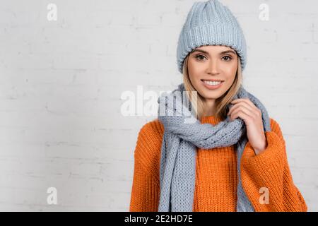 Femme gaie en foulard et chandail chaud près de la brique blanche mur Banque D'Images