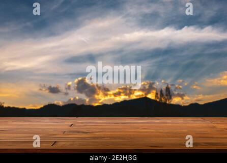 Espace vide de table en bois de planche, vue en perspective, arrière-plan flou de la montagne et ciel bleu large au coucher du soleil, lumière dorée et beau c Banque D'Images