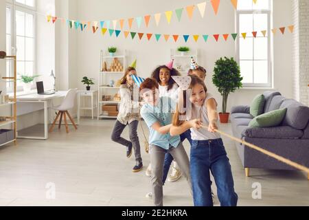 Groupe d'enfants multiethniques heureux jouant la remorqueur de guerre à la fête de plaisir à la maison ou au club enfants Banque D'Images