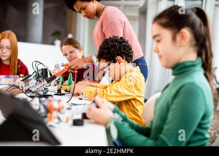 Femme afro-américaine smily enseignant en sciences avec un groupe d'enfants programmation de jouets électriques et de robots dans les salles de classe de robotique Banque D'Images