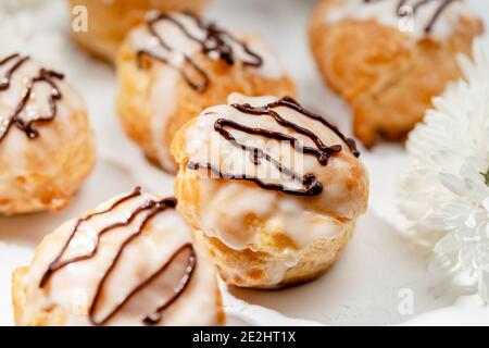Vue en gros plan de délicieux profiteroles frais remplis de crème anglaise sur une table blanche. Des airs savoureux faits maison. Concept de desserts, cuisine de restaurant. Banque D'Images