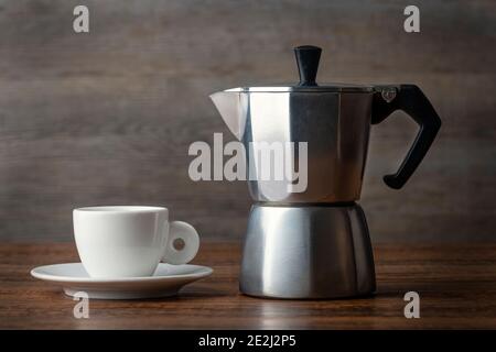 Cafetière expresso traditionnelle à moka et une tasse et une soucoupe sur une table en bois. Banque D'Images