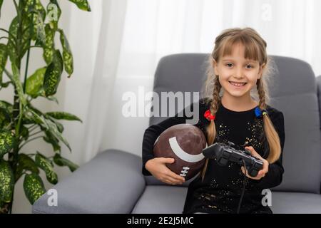 Petite fille tenant un ballon de rugby et un joystick pour jouer jeux vidéo Banque D'Images