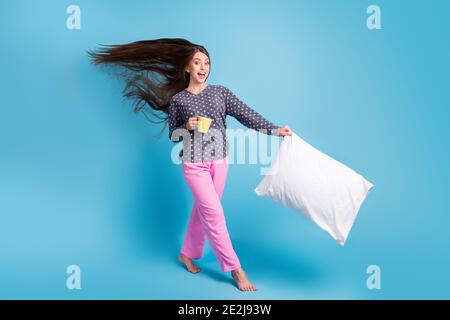 Photo pleine longueur de la belle adolescente air souffle long coiffure pieds nus tenir tasse oreiller dormir-dessus excitée porter chemise à pois pantalon de pyjama rose Banque D'Images