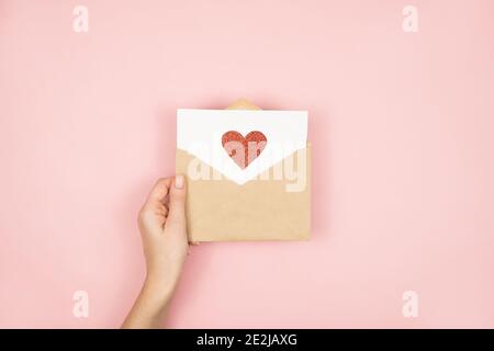 Lettre d'amour dans les mains des femmes sur la Saint Valentin. Carte postale faite à la main avec coeur rouge sur fond rose. 14 février concept. Banque D'Images