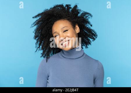 Bonne femme afro souriante, bonne humeur, danse avec ses cheveux bouclés noirs, isolée sur le bleu Banque D'Images