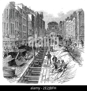 Fleet-Street, approfondissement de l'égout, 1845. Travailleurs améliorant le système souterrain de déchets à Londres, avec Temple Bar au loin. '... la difficulté de garder ouvert le trafic, de manière à ne pas éteindre "l'aspect très animé" de Fleet-Street, est un travail de beaucoup de difficulté. Le coût de la présente entreprise, sous contrat de MM. Ward et son, de la rue Aldersgate, est &#xa3;2000...il ne semble pas y avoir de données publiées qui permettent de déterminer l'étendue totale des égouts métropolitains. Les divisions de Holbom et de Finsbury comptent quatre-vingt-cinq miles. En plus de Banque D'Images