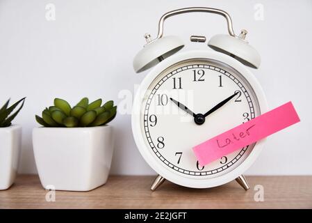 Notion de temporisation et de procrastination. Pense-bête avec mot plus tard sur le réveil blanc. Heure d'urgence Banque D'Images