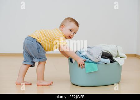 Un petit garçon pousse le panier avec du linge propre après le lavage Banque D'Images