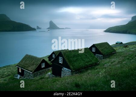 Vue pittoresque sur les maisons couvertes d'herbe de faroese, dans le village de Bour. Drangarnir et Tindholmur des piles de mer en arrière-plan. Île De Vagar, Îles Féroé, Danemark. Photographie de paysage Banque D'Images