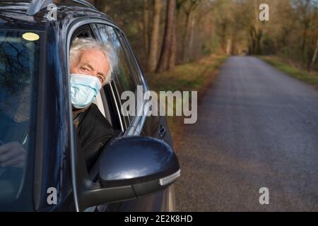 Homme aîné avec un masque facial en voiture sur la route Banque D'Images