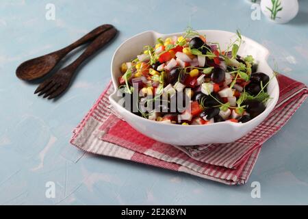 Salade de haricots noirs, maïs, bâtonnets de crabe et petits pois dans un bol blanc sur fond bleu clair Banque D'Images