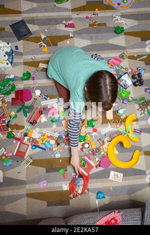 Une jeune fille s'est assise sur le sol du salon pour jouer avec les jouets playmobil Banque D'Images