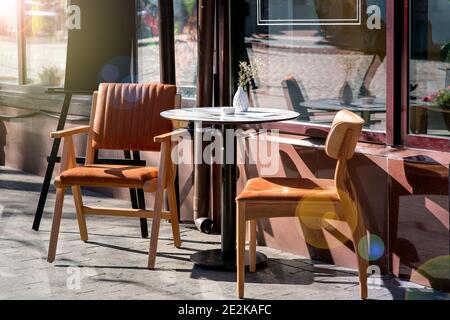 une table ronde avec deux chaises avec dos sur les pattes en bois d'un café d'été sur le trottoir près de la façade du bâtiment avec des fenêtres panoramiques de Banque D'Images