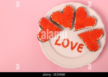 Canape avec caviar rouge et fromage à la crème en forme de coeur pour la Saint-Valentin sur fond rose. Vue de dessus Banque D'Images