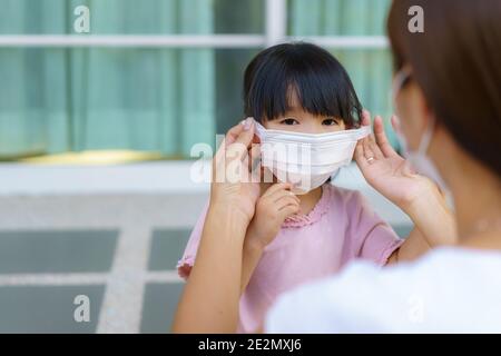 La mère asiatique aide sa fille à porter un masque de protection pour protéger la situation d'épidémie de coronavirus Covid-19 avant d'aller à l'école. Préparez-vous à l'école Banque D'Images