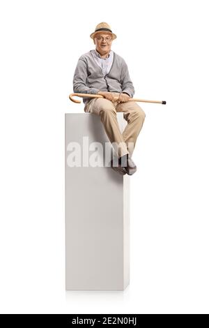 Homme âgé assis sur une colonne et tenant une marche canne isolée sur fond blanc Banque D'Images