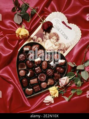 ANNÉES 1980 SAINT VALENTIN COEUR EN FORME DE COEUR CHOCOLATS BOÎTE DE BONBONS PARTIELLEMENT MANGÉ CARTE ANTIQUE ET ROSES SUR FOND ROUGE SATINÉ - KV627 DAS001 HARS BOURGEONS RELATIONS BUD CONCEPT CONNEXION CONCEPTUEL ENCORE LA VIE CHOCOLATS AFFECTUEUX ÉLÉGANT MANGÉ SYMBOLIQUE AFFECTION CONCEPTS PARTIELLEMENT TOGETHERNESS BONBONS REPRÉSENTATION DÉMODÉE Banque D'Images