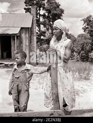 FEMME AFRO-AMÉRICAINE DES ANNÉES 1930 MÈRE ET SON FILS GARÇON DEBOUT AVANT MAISON DE CONSTRUCTION PENCHÉE SUR LA CLÔTURE DE FERME APRÈS ALABAMA USA - N73 HAR001 HARS PENCHÉE VIEILLE MODE PAUVRETÉ 1 STYLE JUVÉNILE PEUR JEUNES ENFANTS ADULTES FAMILLES STYLE DE VIE ARCHITECTURE FEMMES PAUVRES RURAL ACCUEIL VIE COPIE ESPACE DEMI-LONGUEUR FEMMES PERSONNES AGRICULTURE MÂLES ALABAMA BÂTIMENTS AGRICULTURE B&W LIBERTÉ AVANT LES RÊVES RÉSISTANCE À LA PROPRIÉTÉ AFRO-AMÉRICAINS AFRO-AMÉRICAINS ET LES AGRICULTEURS DU SUD-EST DE L'ETHNIE NOIRE AU SUD DE LA CONNEXION IMMOBILIÈRE CONCEPTUELLE LES STRUCTURES EN RETARD DÉSAVANTAGÉES EDIFICE DÉSAFFECTÉ DÉÇU DÉCONNECTÉ APPAUVRI Banque D'Images