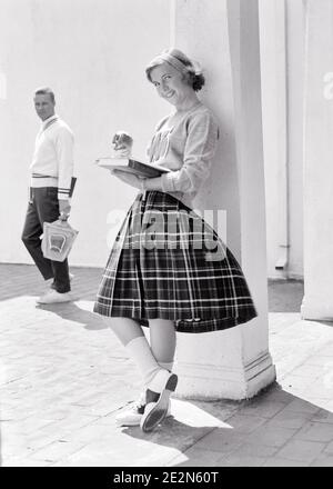 ANNÉES 1950, UNE JEUNE FILLE DES ANNÉES 1960 S'EST PENCHÉE CONTRE LA COLONNE MANGEANT LA LECTURE DE POMME LIVRE REGARDANT L'APPAREIL PHOTO SOURIANT ALORS QUE LE PETIT AMI POTENTIEL PASSE À CÔTÉ - S11457 DEB001 HARS BLONDE PORTANT ÉDUCATION DE L'UNIVERSITÉ APPLE PULL NOSTALGIQUE PAIRE ROMANCE SUBURBAN URBAN VIEUX TEMPS OCCUPÉ AVENIR NOSTALGIE PENCHÉE VIEILLE MODE 1 JEUNE COMMUNICATION BLONDE JEUNE ADULTE ATHLÈTE GAIETÉ HEUREUX JOIE STYLE DE VIE CAMPUS FEMMES SANTÉ ESPACE DE COPIE CONTRE LES PERSONNES PLEINE LONGUEUR PETIT AMI HOMMES ADOLESCENT FILLE ADOLESCENT GARÇON ATHLÉTIQUE BASKETS CONFIDENCE BANDEAU B&W OEIL CONTACT ÉCOLES RÊVES BONHEUR RAQUETTE UNIVERSITÉS GAIES Banque D'Images