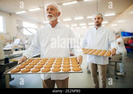 Deux hommes portant des biscuits sur des assiettes dans une usine alimentaire. Banque D'Images