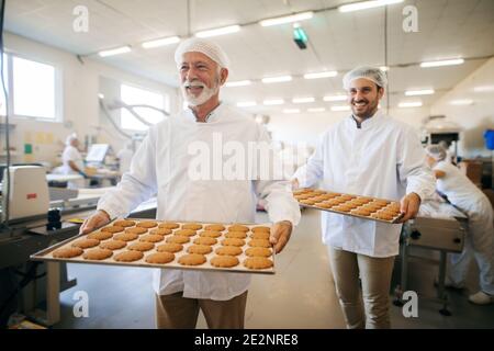 Deux hommes portant des biscuits sur des assiettes dans une usine alimentaire. Banque D'Images