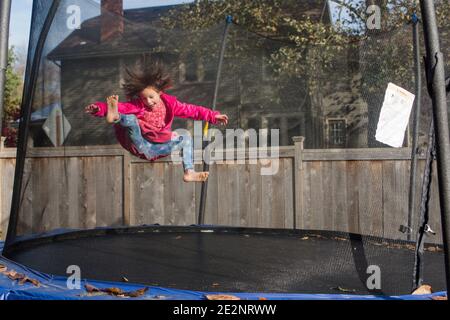 Une petite fille joyeuse avec des sauts de cheveux sauvages sur le trampoline avec filet Banque D'Images