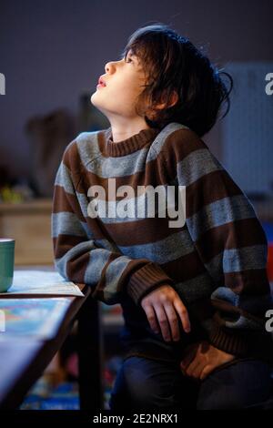 Un beau garçon en chandail confortable est assis à la table en lumière Banque D'Images