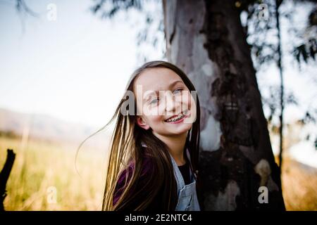 Jeune fille souriant pour l'appareil photo à côté de l'arbre Banque D'Images