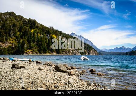 Rive du lac avec rochers, montagnes et pins. Un bateau à moteur flottant près d'une bouée. Été à Bariloche. Banque D'Images