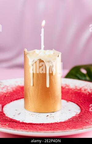 gâteau de Pâques doré avec une bougie sur fond rose avec des feuilles tropicales Banque D'Images