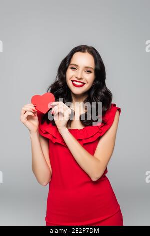 jeune femme gaie en robe tenant le coeur de papier rouge isolé en gris Banque D'Images