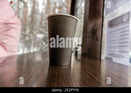 Une tasse de café en papier noir est placée sur un bar comptoir dans un café donnant sur l'hiver enneigé Banque D'Images