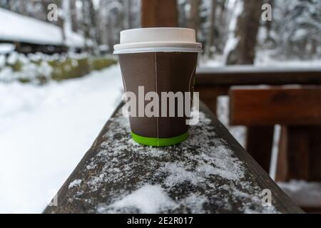 Un gobelet en papier avec couvercle en plastique se tient sur le belvédère sur fond de forêt enneigée en hiver Banque D'Images
