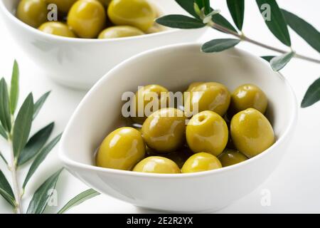 Olives salées et branches d'olive placées sur un fond blanc Banque D'Images