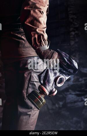 Photo de la main de l'étalon dans la veste et les gants tenant le vieux masque de gaz en caoutchouc solviet sur fond de briques détruites. Banque D'Images