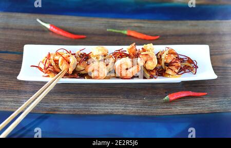 Crevettes grillées aux oignons et au piment sur une assiette blanche sur la table. Pour un menu asiatique Banque D'Images