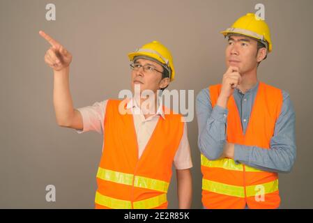 Deux jeunes hommes asiatiques ouvriers du bâtiment ensemble sur fond gris Banque D'Images