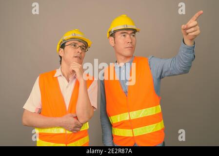 Deux jeunes hommes asiatiques ouvriers du bâtiment ensemble sur fond gris Banque D'Images