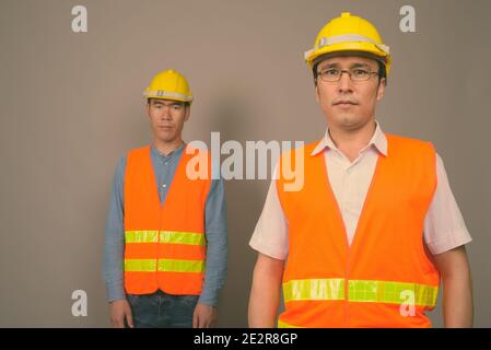 Deux jeunes hommes asiatiques ouvriers du bâtiment ensemble sur fond gris Banque D'Images