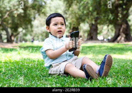 Les nouvelles technologies numériques entre les mains d'un enfant. Petit garçon jouant avec un téléphone mobile dans le parc en automne Banque D'Images