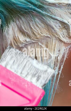 Gros plan du coiffeur à l'aide d'une brosse rose tout en appliquant de la peinture à la cliente féminine avec la couleur de cheveux émeraude, pendant le processus de blanchiment des racines de cheveux en ha Banque D'Images