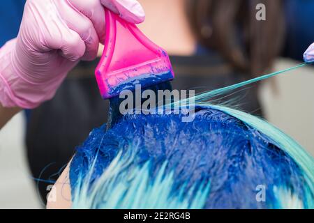 Coiffeurs professionnels en gant de protection à l'aide de la brosse rose tout en appliquant la peinture bleue à la femme avec couleur de cheveux émeraude, processus de teinture des cheveux Banque D'Images