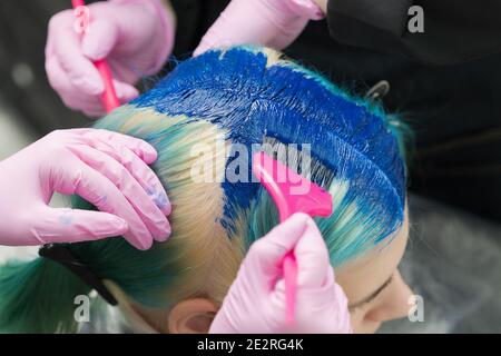 Coiffeurs utilisant la brosse rose tout en appliquant la peinture bleue à la femme client avec une couleur de cheveux émeraude pendant le processus de teinture cheveux de couleur unique Banque D'Images