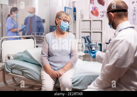 Médecin d'expliquer la radiographie à une femme sénior malade dans la salle de consultation au cours de la pause de covidout. Médecin vérifiant les poumons du patient regardant la radiographie pendant une pandémie de coronavirus. Banque D'Images